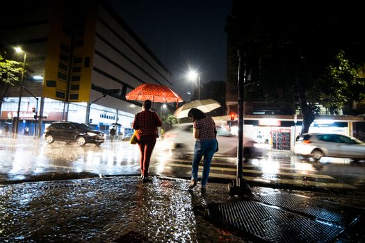 Pedestrians with umbrellas walking in the rain at night on an urban street.