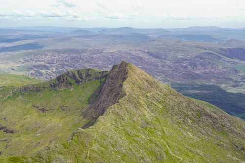 Free Breathtaking aerial view of a rugged green mountain summit with expansive valley in the background. Stock Photo