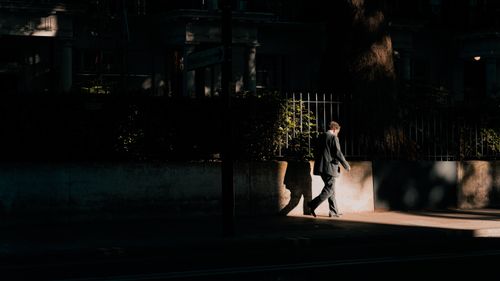 Free A man in a suit walks on a sunlit city sidewalk, casting a shadow. Stock Photo