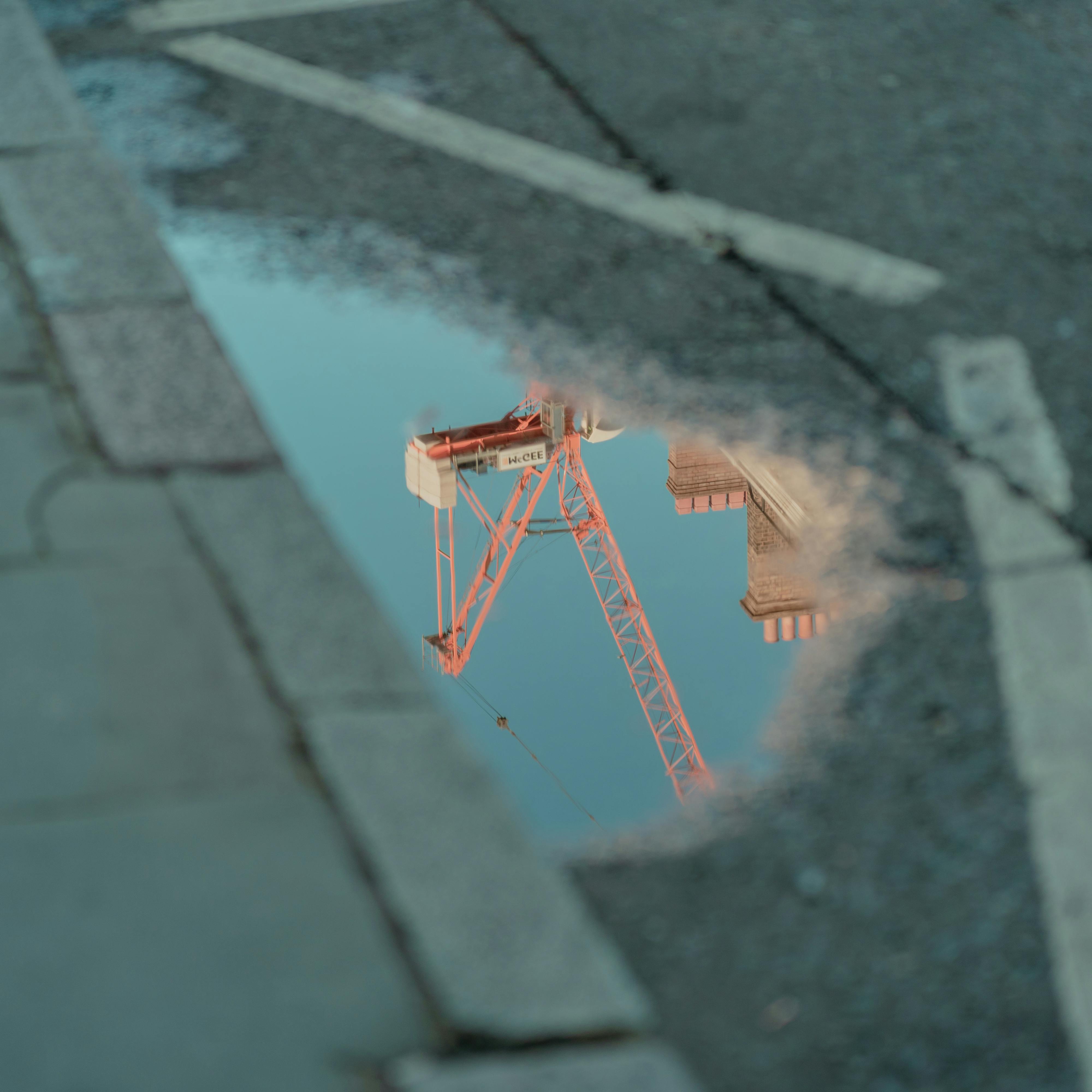 Reflection of a construction crane in a puddle on a city street, capturing industrial urban life.