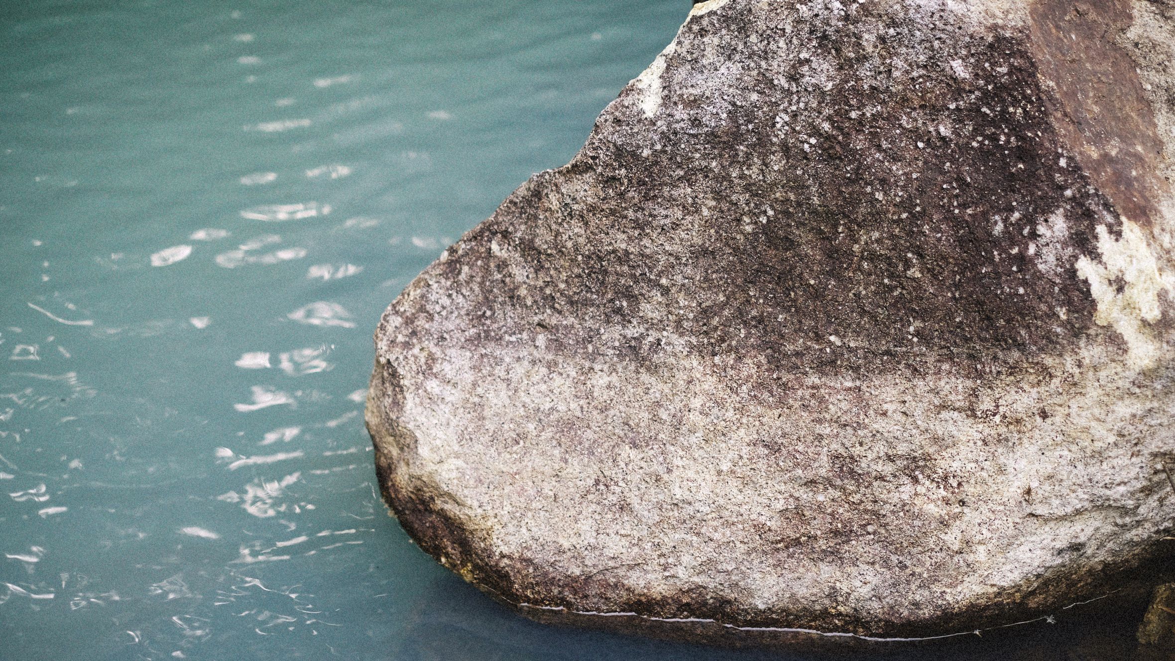 Detailed view of a textured rock emerging from calm turquoise water, exuding serenity.