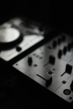 Close-up of a DJ mixer in low light, highlighting its controls and dark ambiance.