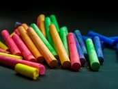 黑色表面上排列着一系列彩色粉笔棒，非常适合艺术和教育主题