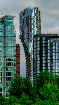 A striking view of Vancouver's modern twisting skyscraper amidst green foliage at dusk.