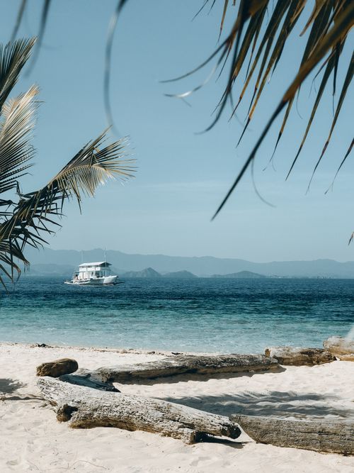 Free Peaceful tropical beach scene with a sailboat on the horizon. Stock Photo