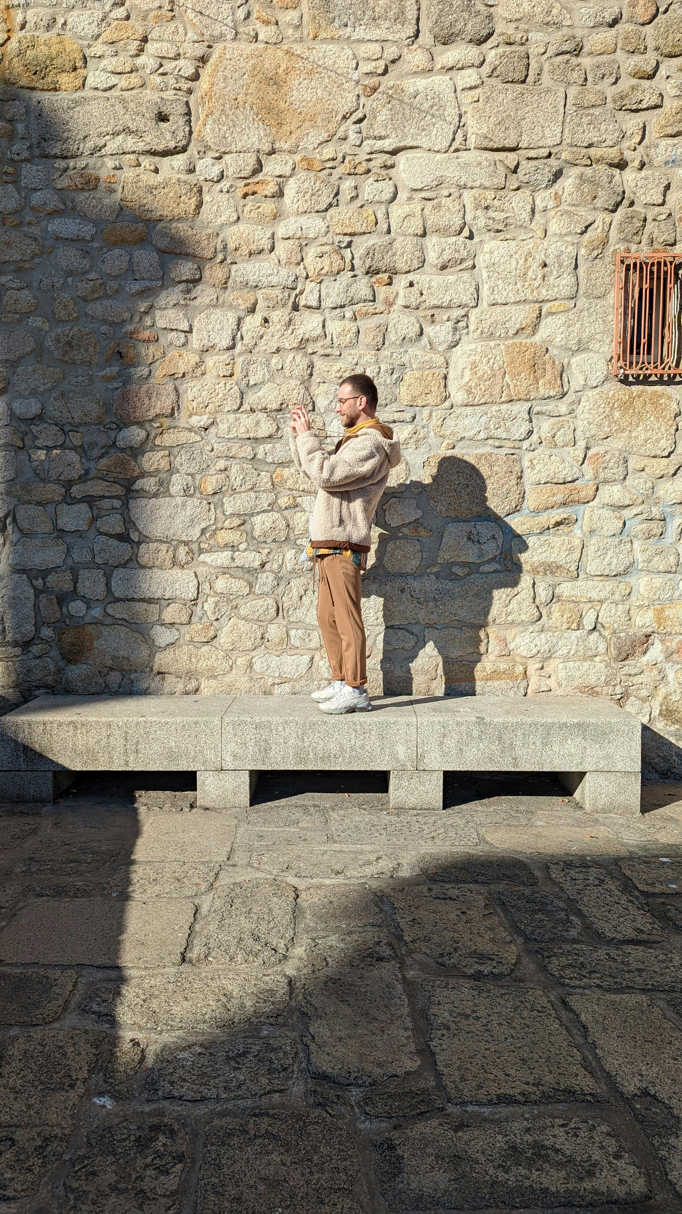 A man captures his shadow on a stone wall outdoors, showcasing urban exploration and photography artistry.