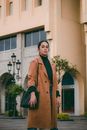 Woman in Brown Coat Standing Near White Concrete Building