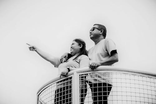 Grayscale Photo of Man and Woman Standing Close to Each Other While Looking Afar 