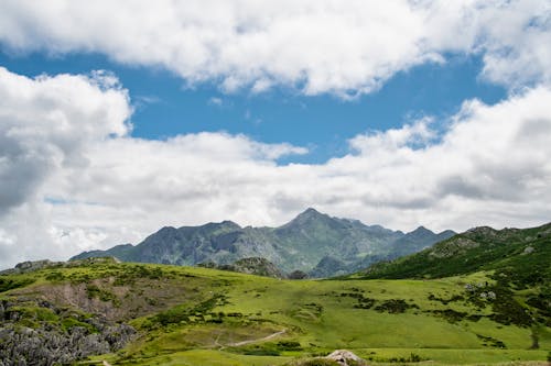 Free Green Grass Field and Mountains Under Blue Sky and White Clouds Stock Photo