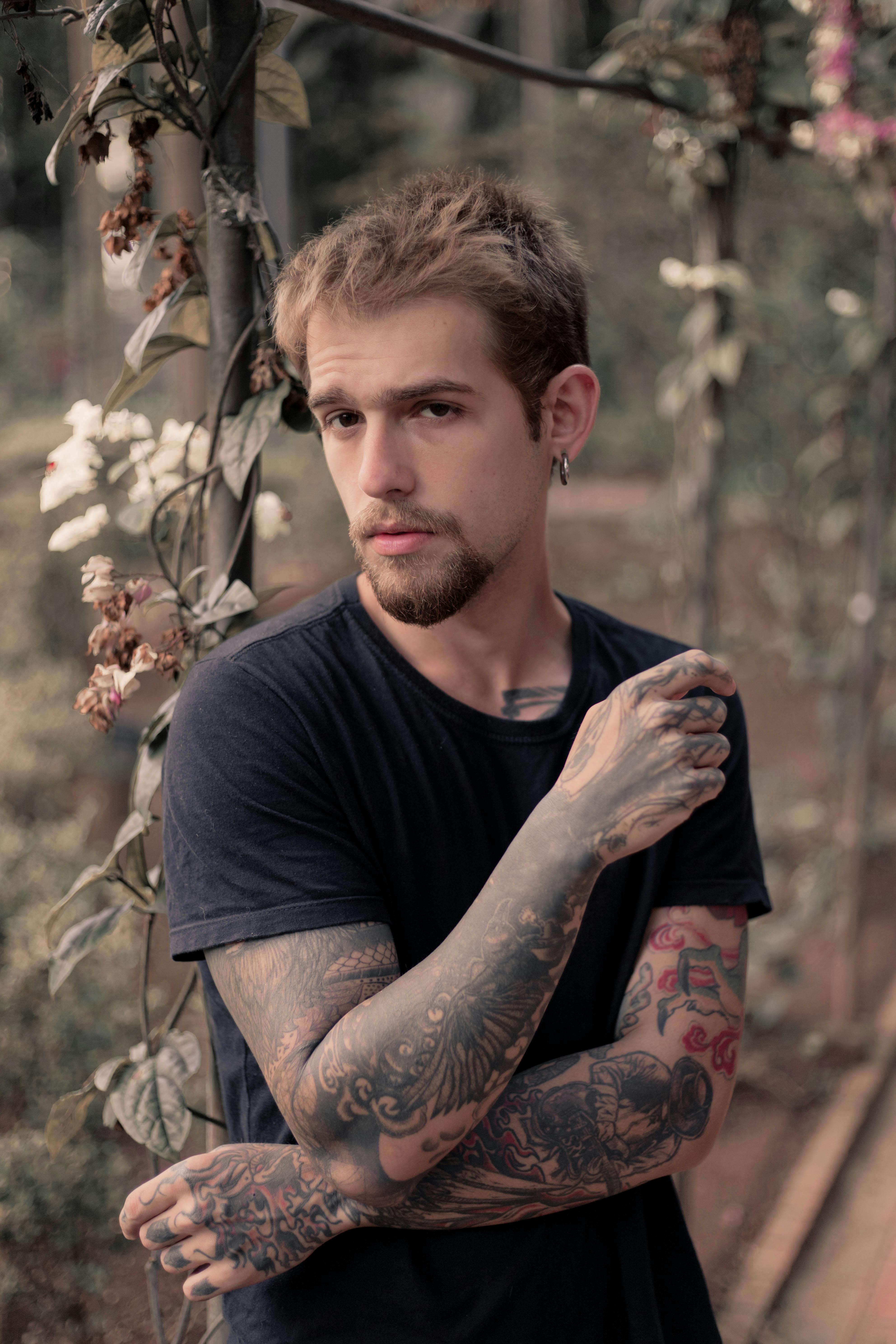 tattooed blonde man with beard standing in garden