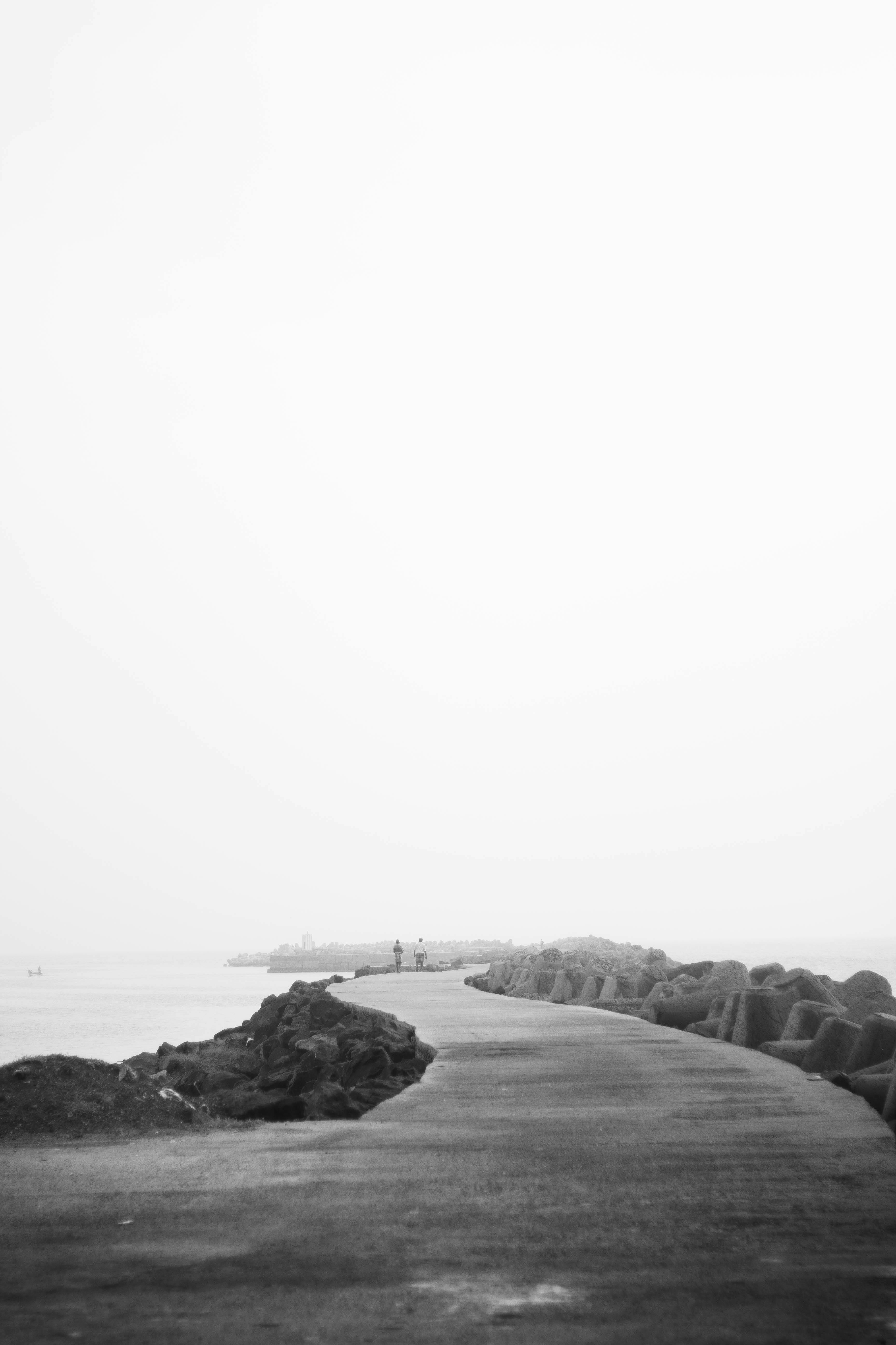 Tranquil scene of people walking on a rocky coastal pathway in grayscale.