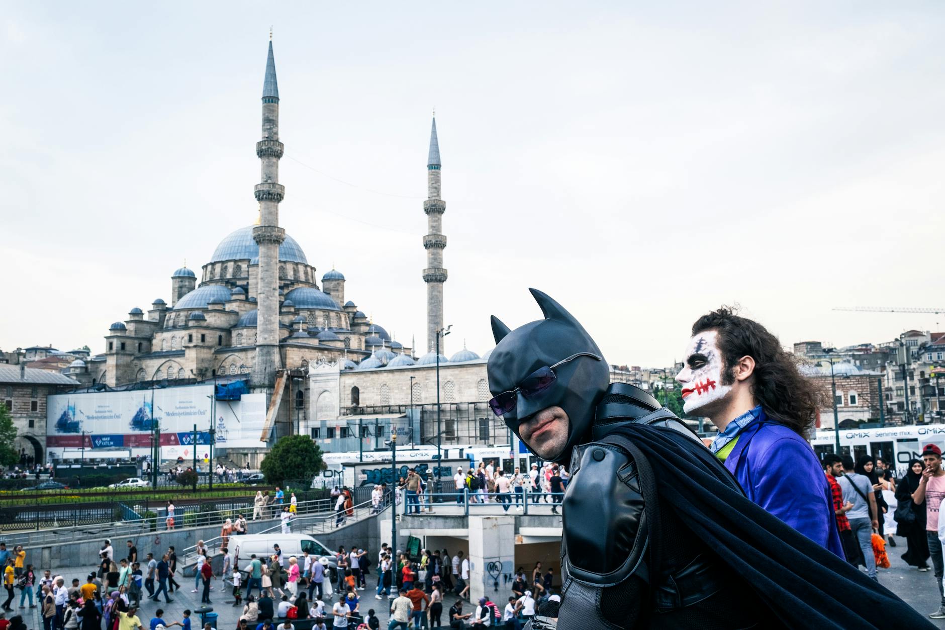 How to Read Batman Without Getting Lost in His Complex History 4 Cosplayers dressed as Batman and Joker in front of Istanbul's iconic Suleymaniye Mosque, a vibrant street scene.