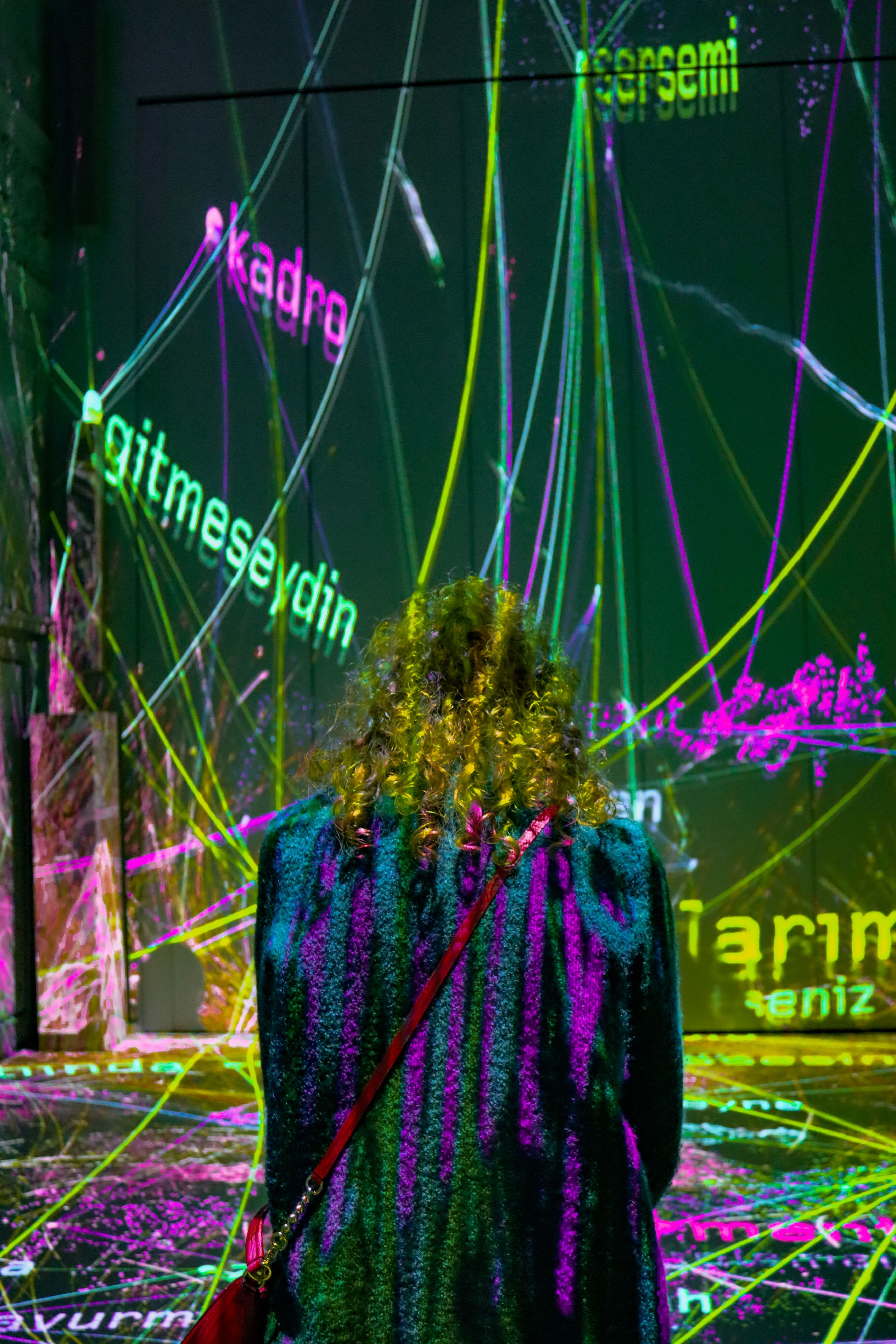 A woman stands facing a colorful neon light installation, creating a vivid and immersive experience.