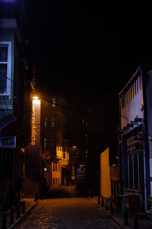 Free An atmospheric night scene of a narrow urban alley illuminated by street lights and shadows, showcasing architecture. Stock Photo