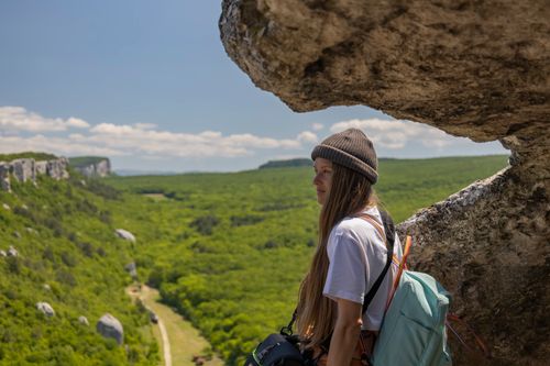 Free Woman hiking on a cliffside with a vast green landscape in view, perfect for adventure travel themes. Stock Photo
