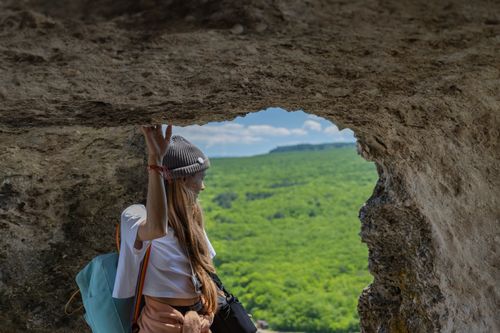 Free A woman in active wear explores a cave with a breathtaking view of lush greenery. Stock Photo