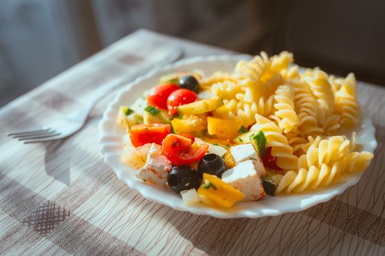 Plate of fusilli with feta cubes, cherry tomatoes, yellow pepper and black olives