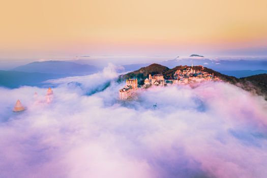 Majestic aerial shot of a castle on a mountainous landscape shrouded in mist during sunrise.