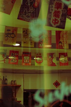 A window view of a Japanese-themed coffee shop featuring vibrant decorations and Maneki-neko motifs.