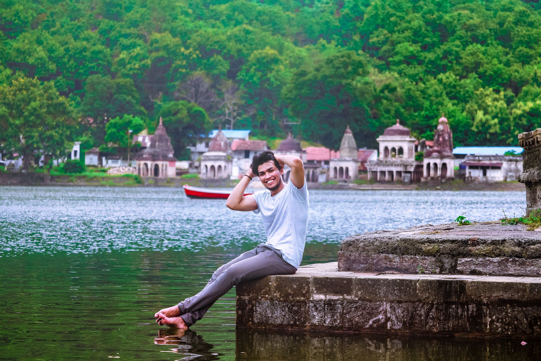 Cheerful man sitting by a serene riverside with historic temples in the background, Maharashtra, India.