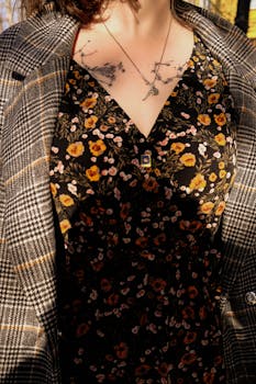 Close-up of woman wearing a floral dress and plaid jacket, showcasing floral tattoos and necklace.