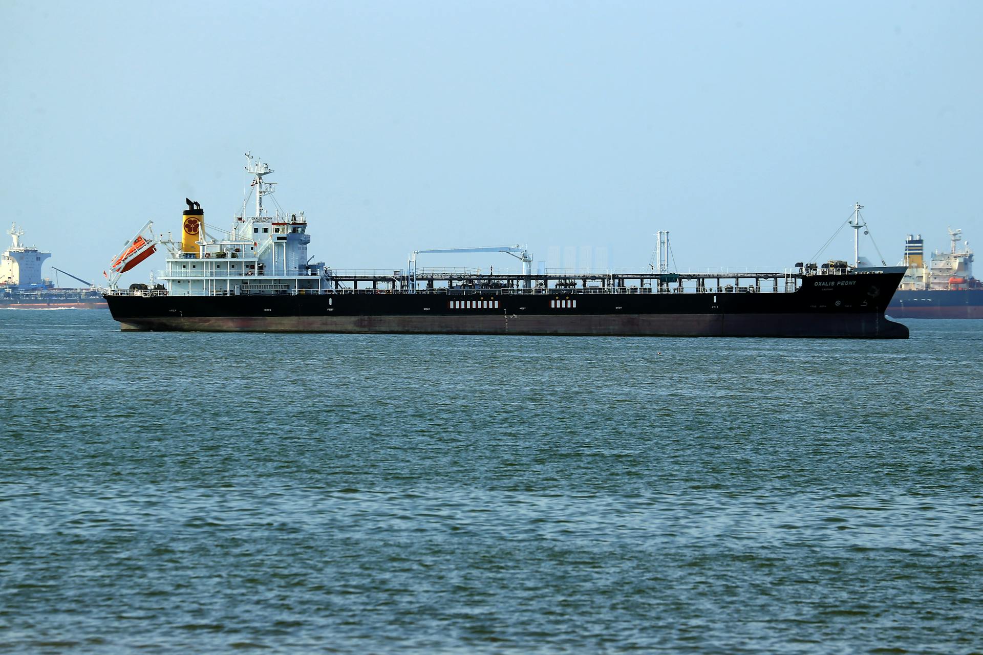 Oil tanker navigating calm ocean waters near a coastal harbor. Clear day view.