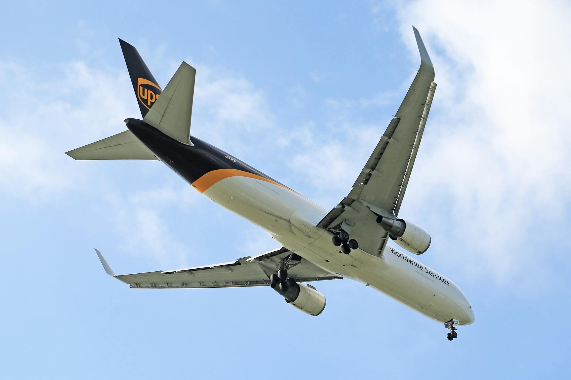 A cargo aircraft flying against a backdrop of a clear blue sky, showing its wings and landing gear.