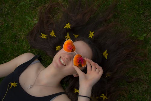 Woman Holding Her Orange Sunglasses While Laying Down on Grass