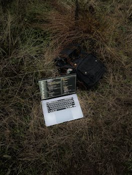 Open laptop displaying code on a grassy field beside a backpack, capturing tech lifestyle outdoors.