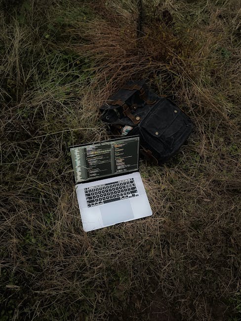 Open laptop displaying code on a grassy field beside a backpack, capturing tech lifestyle outdoors.