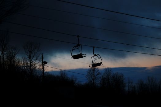 Dramatic silhouette of a ski lift at twilight with a moody sky backdrop, capturing serene dusk scenery.
