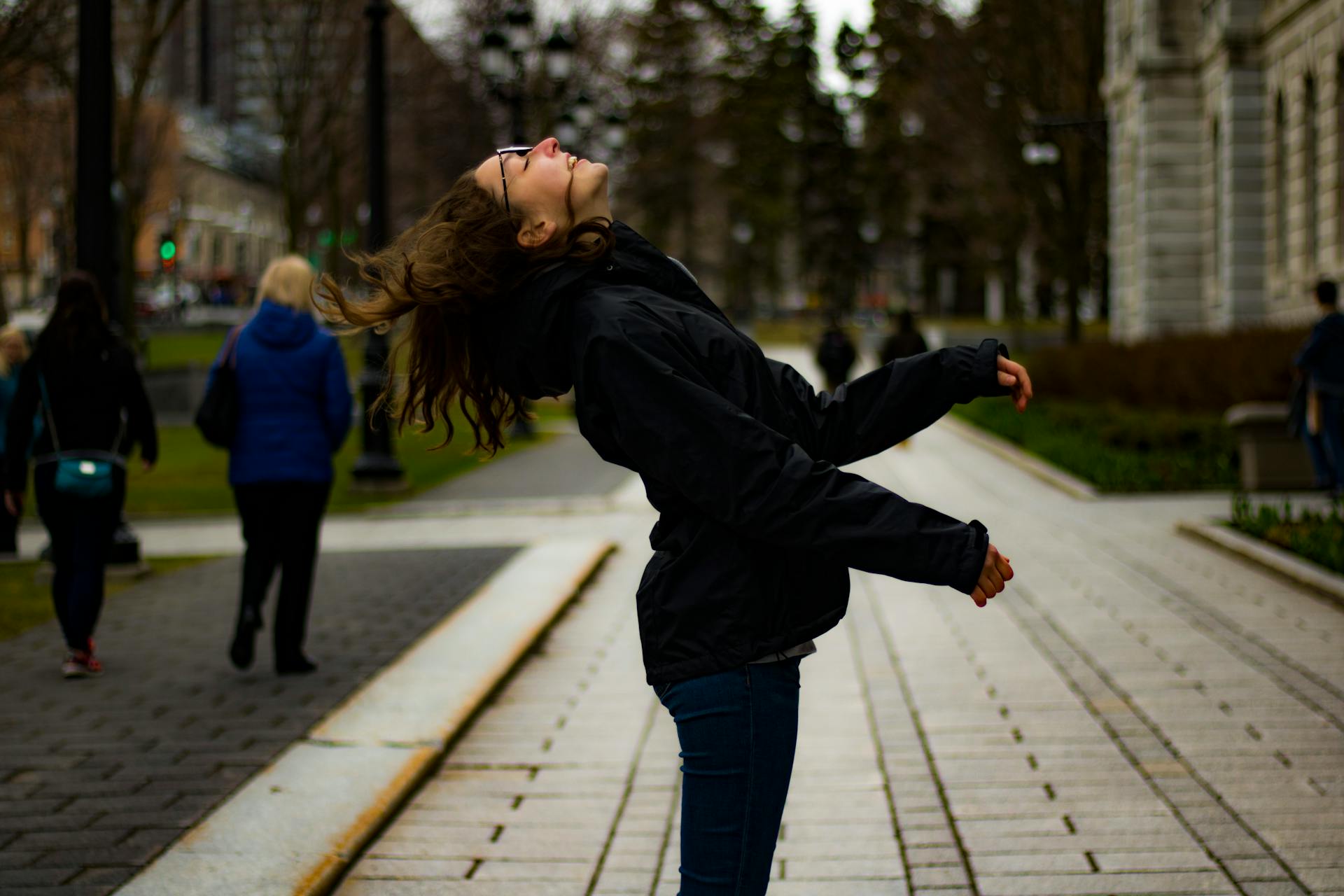 A joyful young woman flips her hair while walking in a city park during the day.