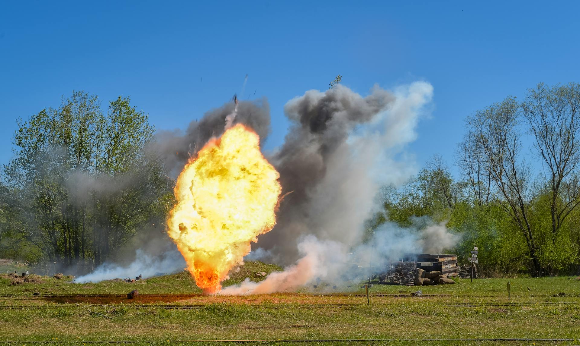 Dramatic explosion with smoke and flames in a rural field under clear blue sky.