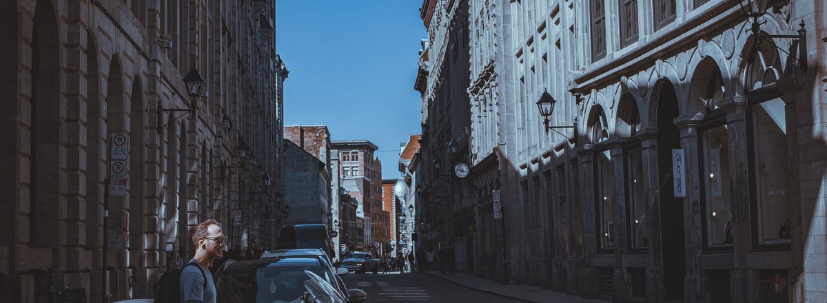 A man walking by a motorcycle on a shadowy street in Old Montreal with historic facades.