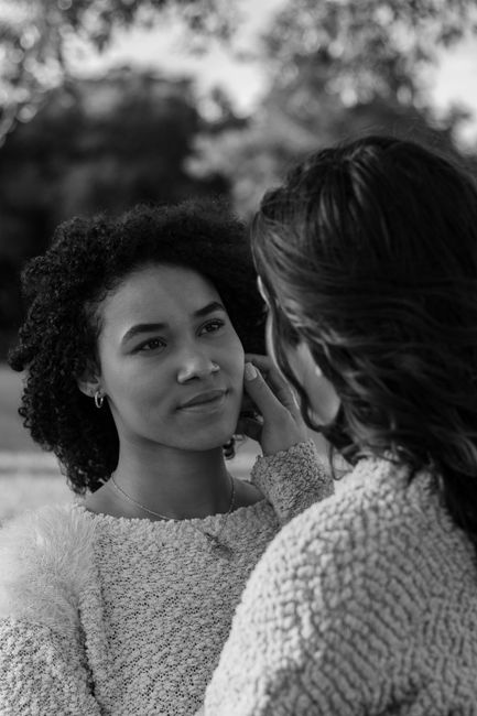 Black and white portrait capturing a tender moment between diverse women in a natural setting.