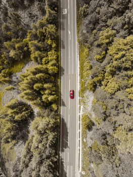 Aerial shot of a red car driving through a forest road in Yorkshire, England.