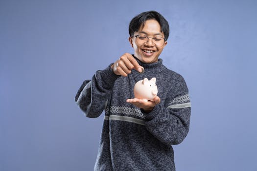 Smiling man holding a piggy bank and inserting a coin, representing savings and financial planning.