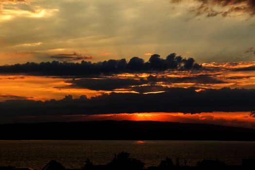 A stunning sunset with dramatic clouds over a calm lake, capturing a serene landscape.