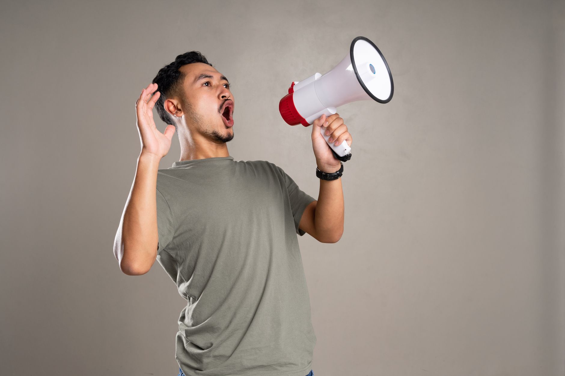 Asian man passionately shouting into a megaphone indoors, conveying energy and excitement.
