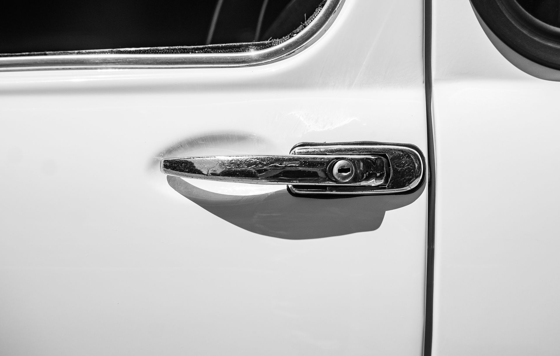 Monochrome close-up of a vintage car door handle in metallic tones.