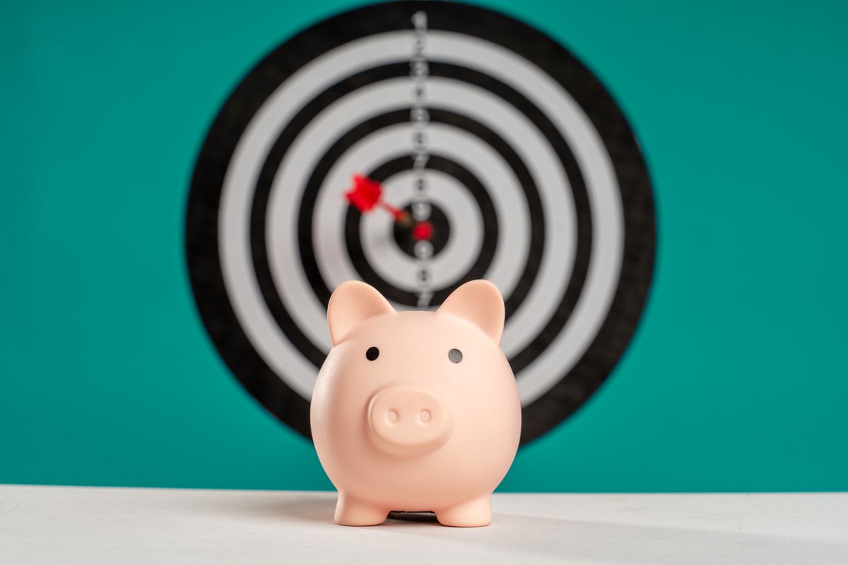 Piggy bank with a dartboard target in the background, representing hitting a daily income target like $373 a day