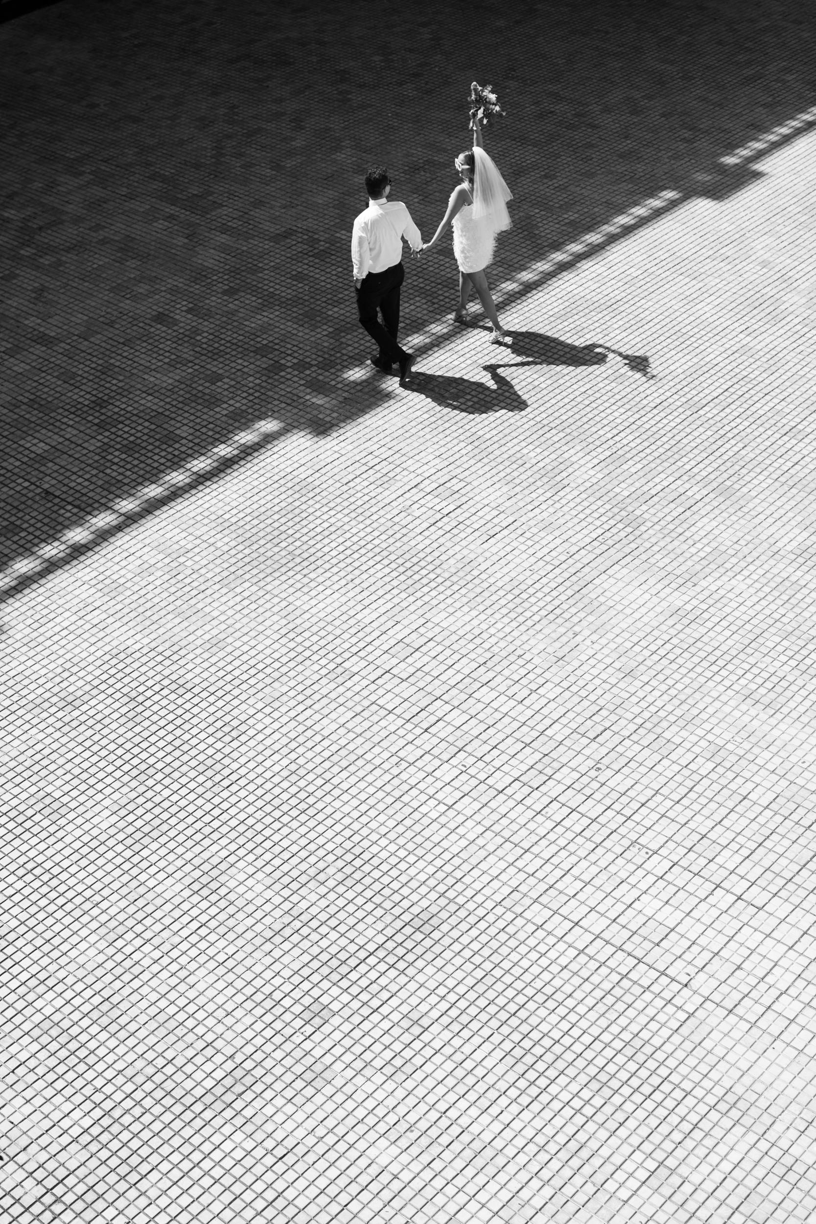 Timeless black and white aerial shot of a couple holding hands on a tiled surface.