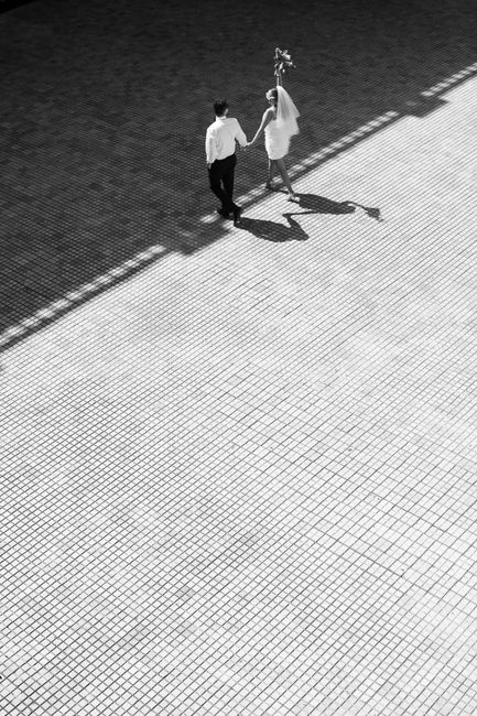Timeless black and white aerial shot of a couple holding hands on a tiled surface.