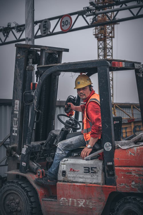 Free Man in Orange Jacket and Black Pants Sitting on Black and Gray Heavy Equipment Stock Photo