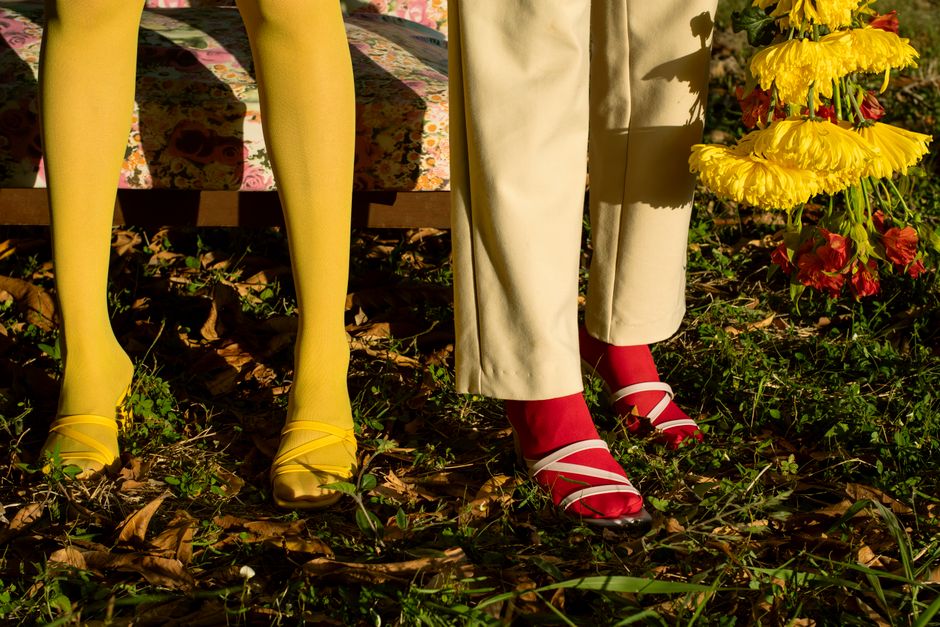 Close-up of two models wearing colorful sandals and tights outdoors surrounded by flowers.