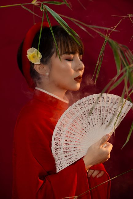 Elegant portrait of an Asian woman in a red kimono holding a decorative fan, against a rich red background.