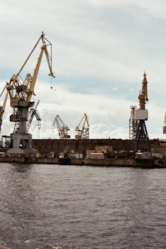 A bustling harbor featuring towering cranes along the waterfront under a cloudy sky.