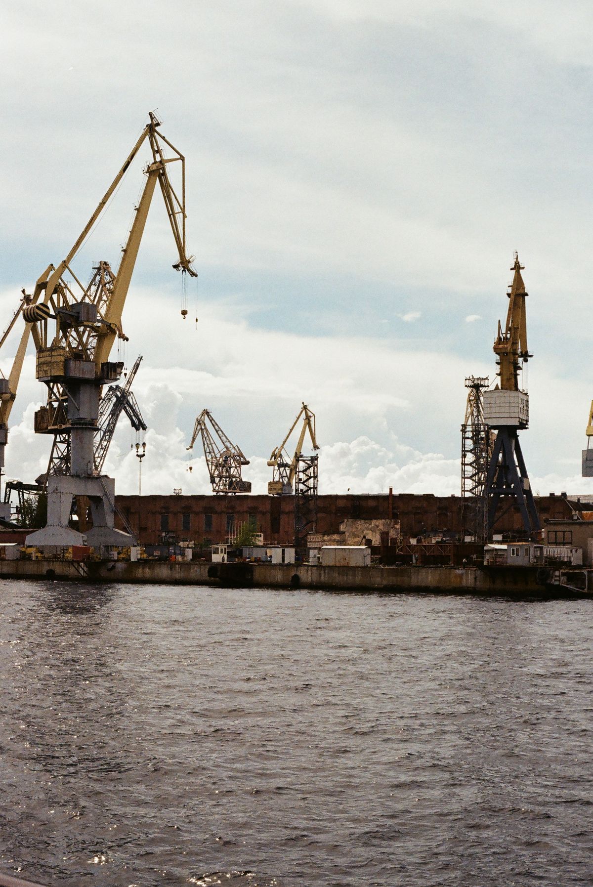 Harbour cranes along a river under a cloudy sky