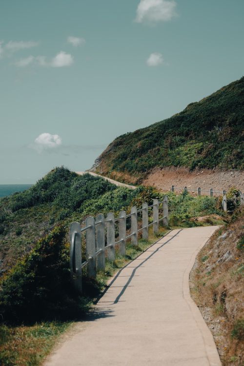 Free A serene coastal pathway bordered by mountains, perfect for summer walks. Stock Photo