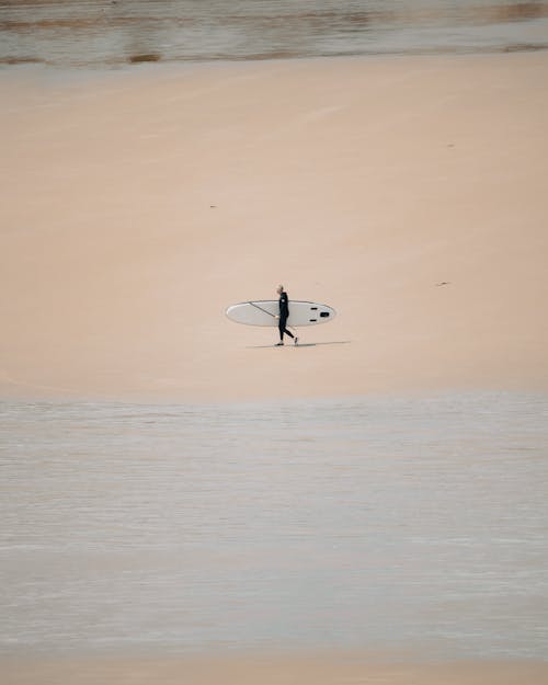 Person Walking on Shore Carrying a Surfboard